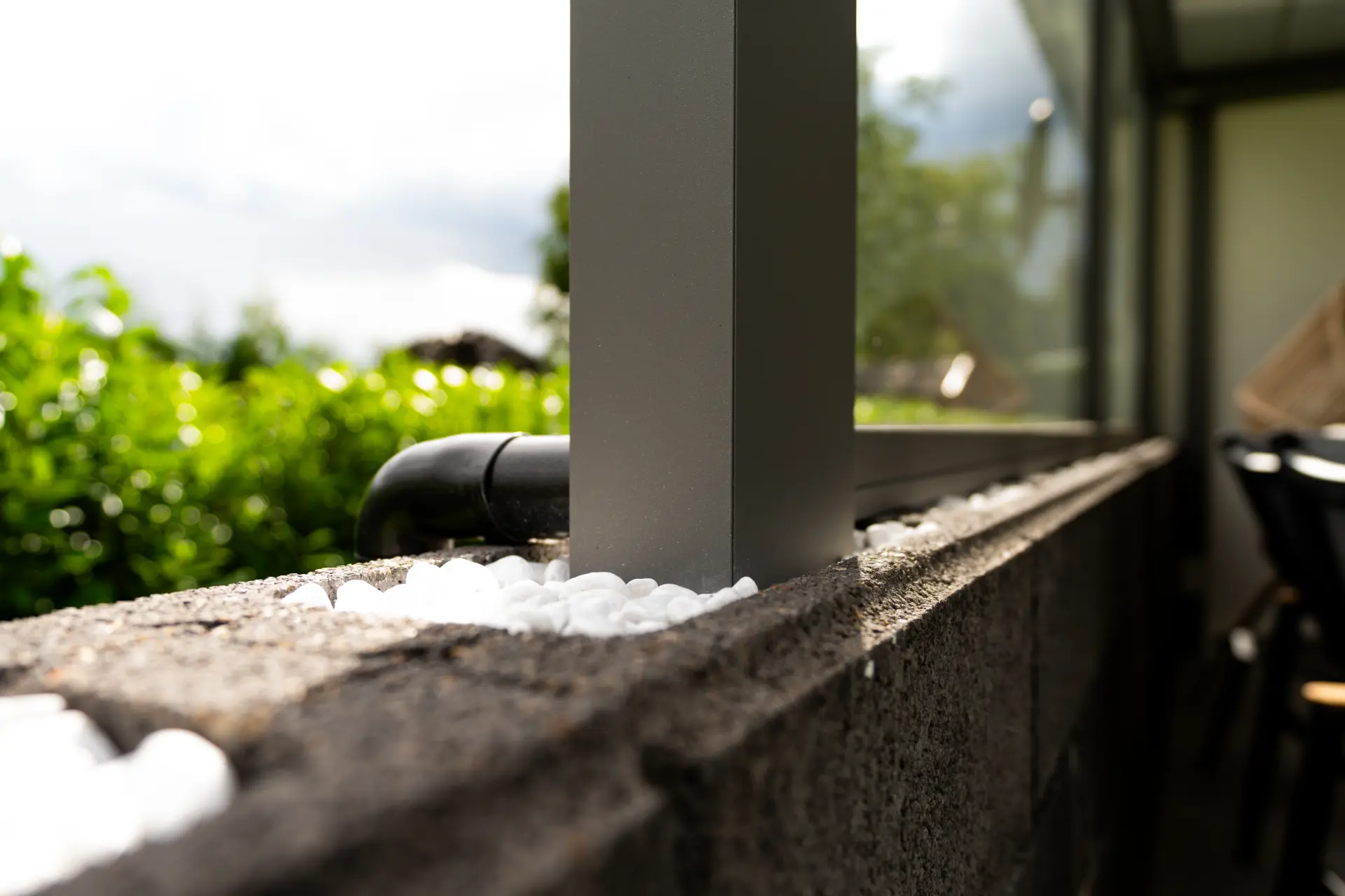 Pfostenfuß eines Terrassendachs auf Natursteinmauer mit weißem Ziersplitt