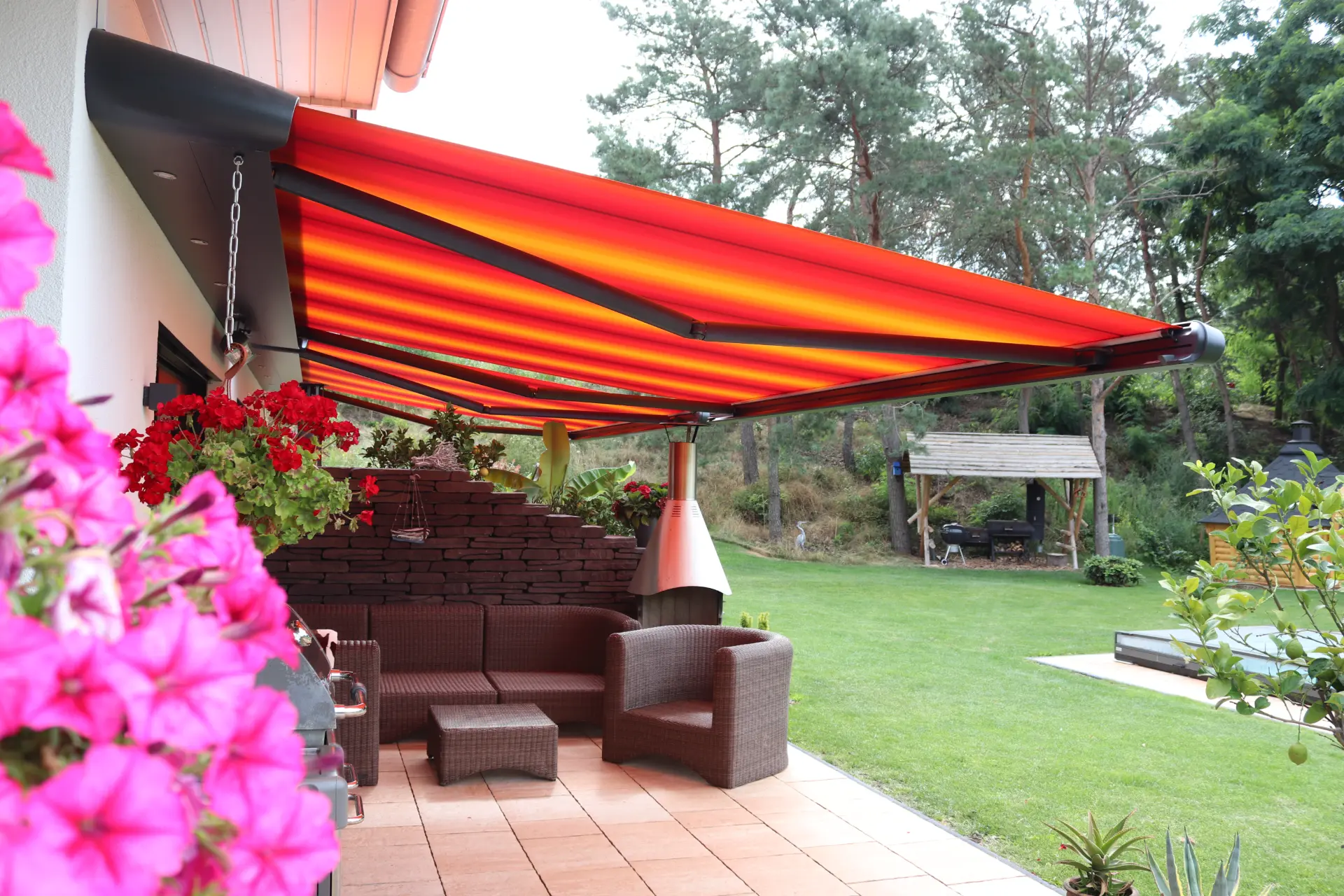 Markise über einer Terrasse mit Rattanmöbeln und blühenden Petunien