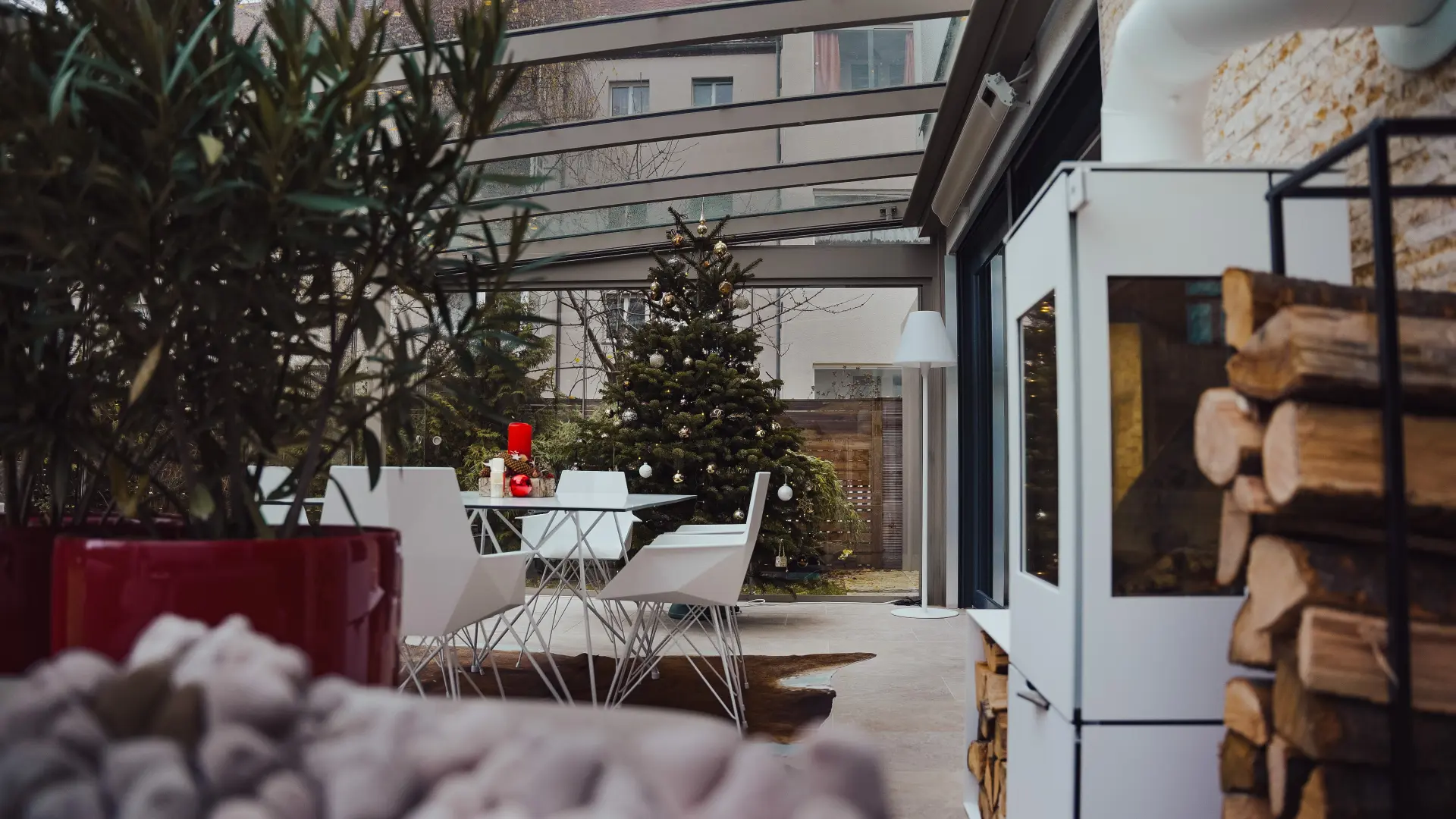 Wintergarten mit Kaminofen, Holzstapel und weißen Designer-Stühlen im Abendlicht