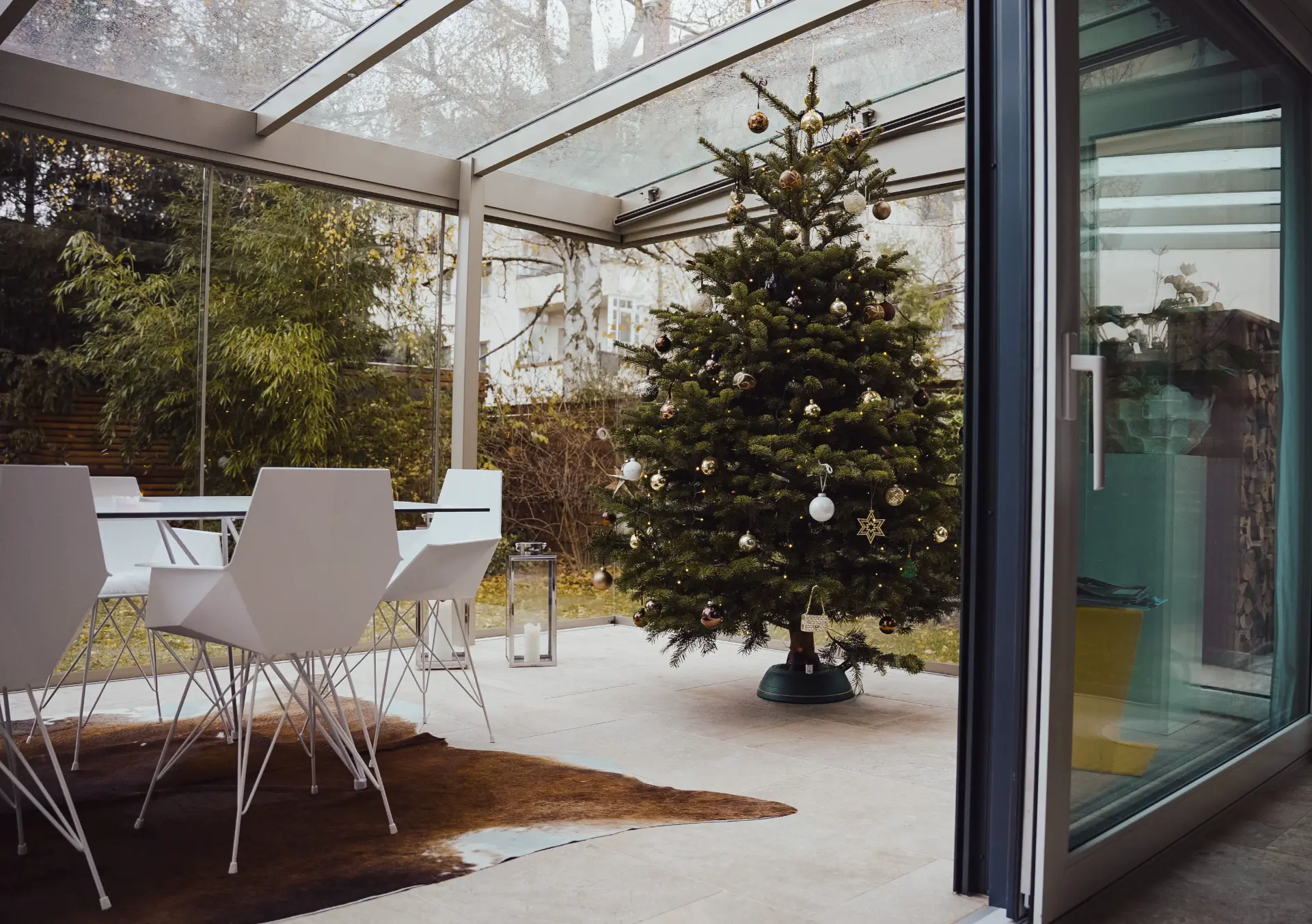 Wintergarten mit geschmücktem Weihnachtsbaum und Blick in den winterlichen Garten