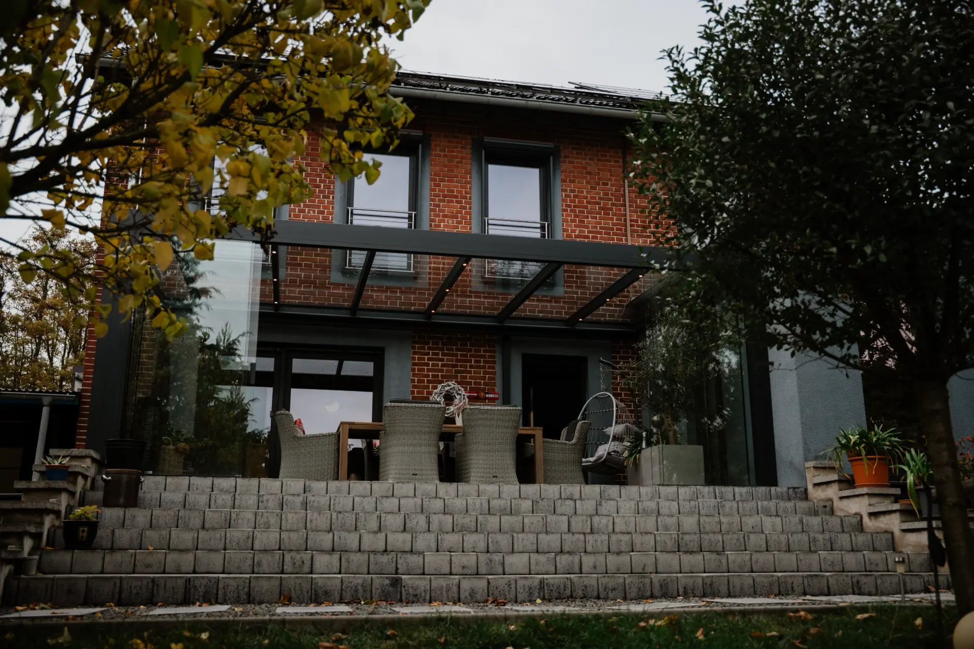 Terrassendach an einem roten Backsteinhaus im Herbst, darunter eine Rattan-Essgruppe