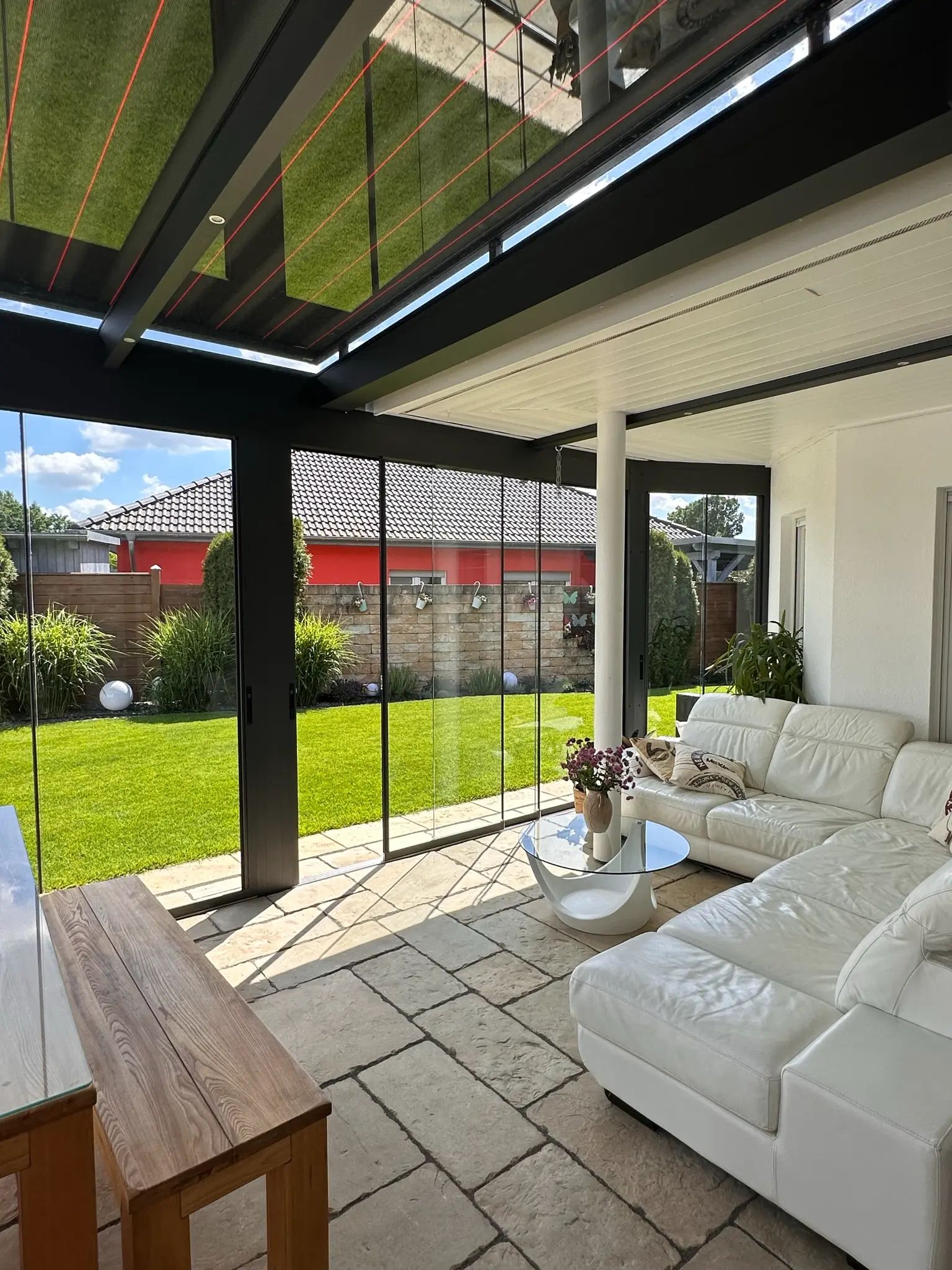 Verglaste Terrasse mit weißem Ledersofa und teils geöffneten Glasschiebewänden