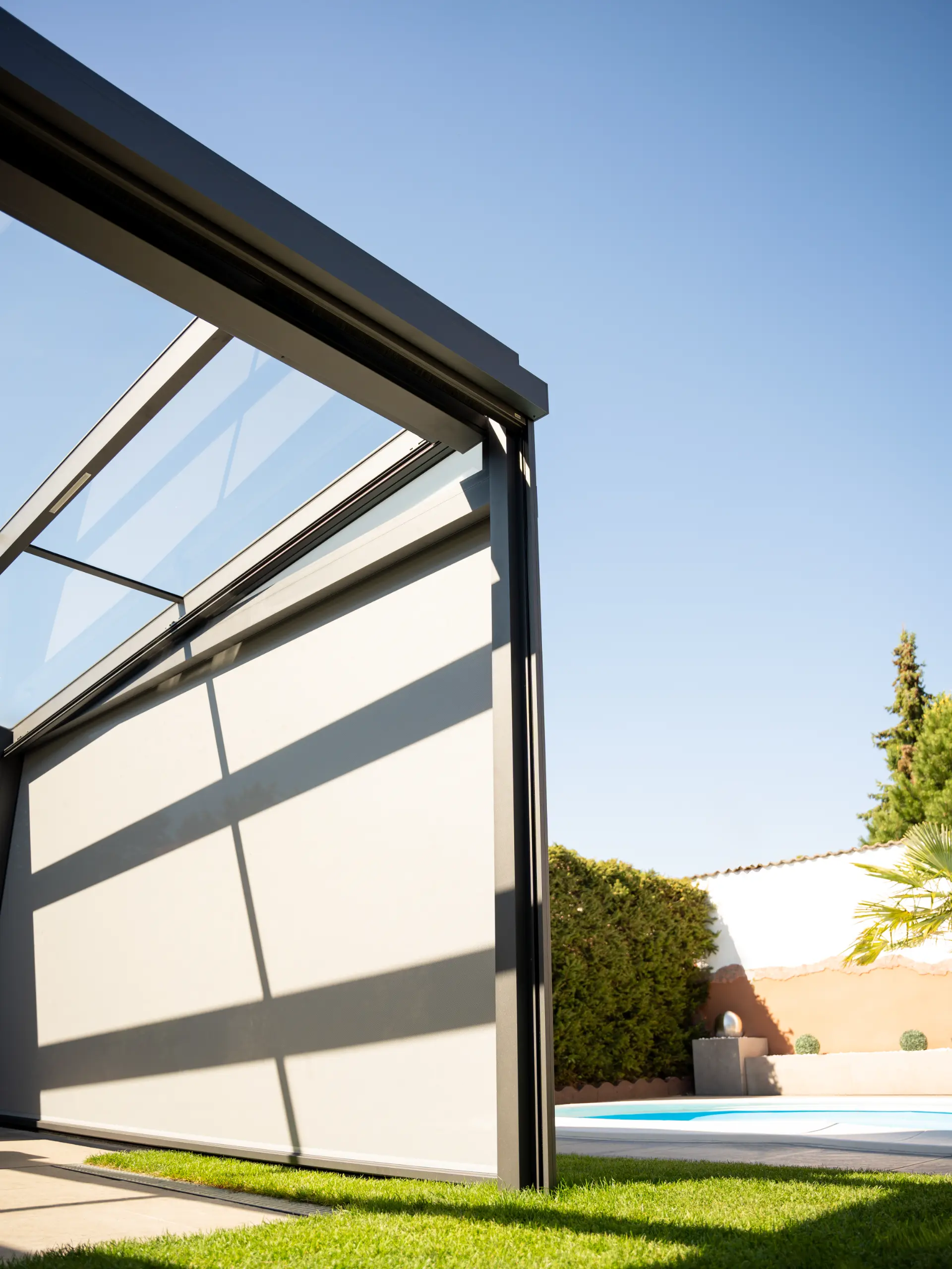 Eckpfosten einer Glasveranda mit geschlossenem Sonnenschutz-Screen vor blauem Himmel