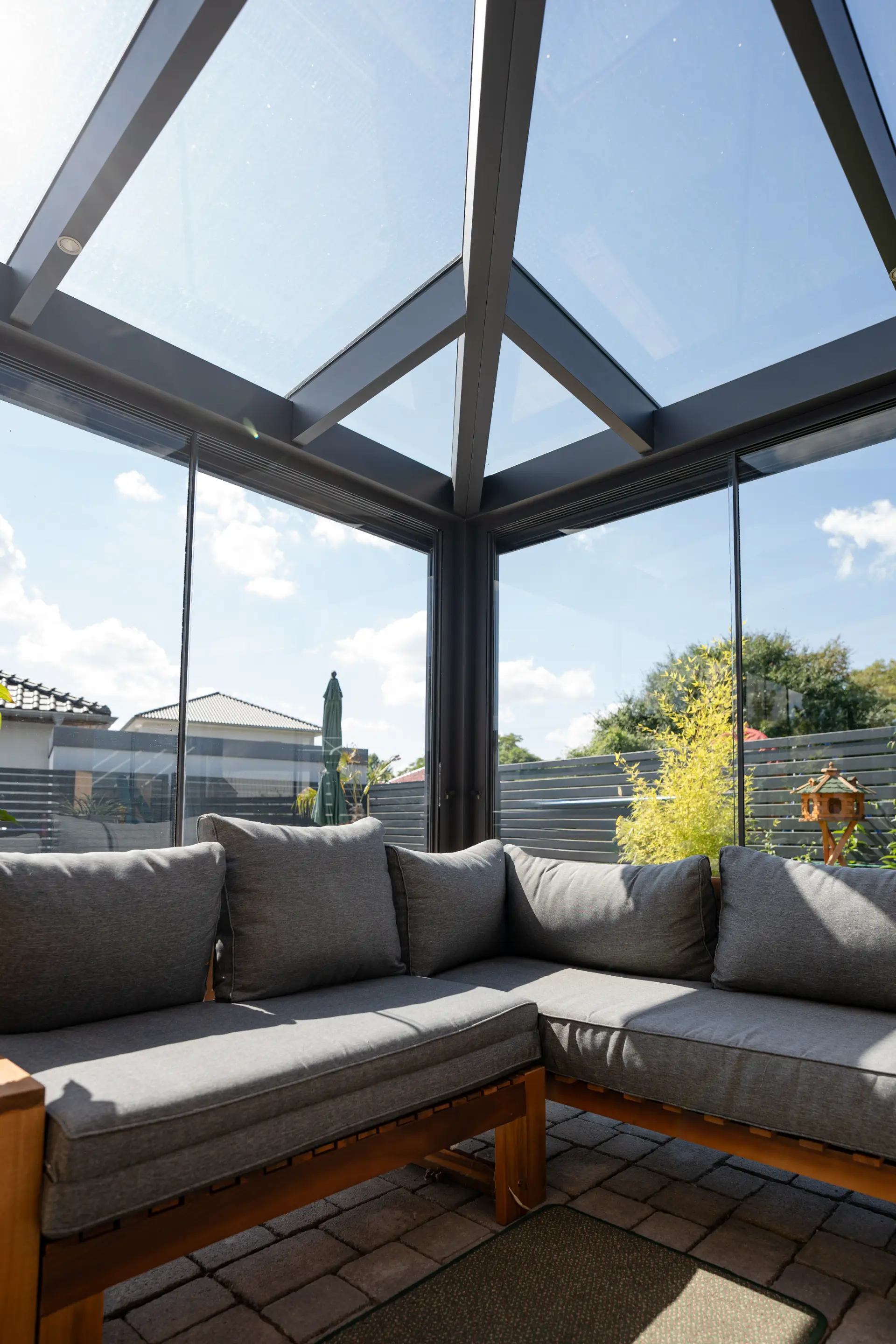 Vollverglaste Wintergarten-Ecke mit grauer Sitzbank und Blick in den Garten