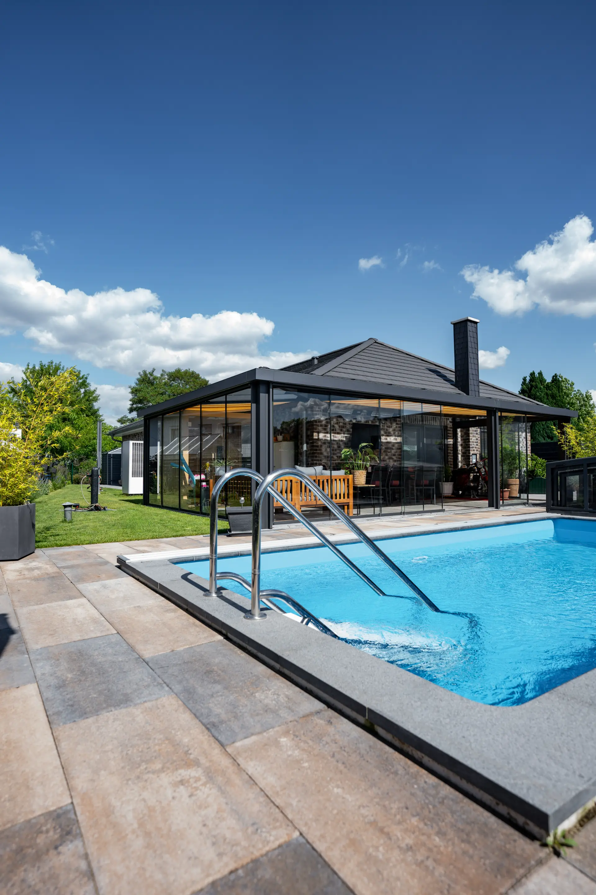Freistehende Glasveranda am Pool im Gegenlicht, dahinter ein Gartenhaus