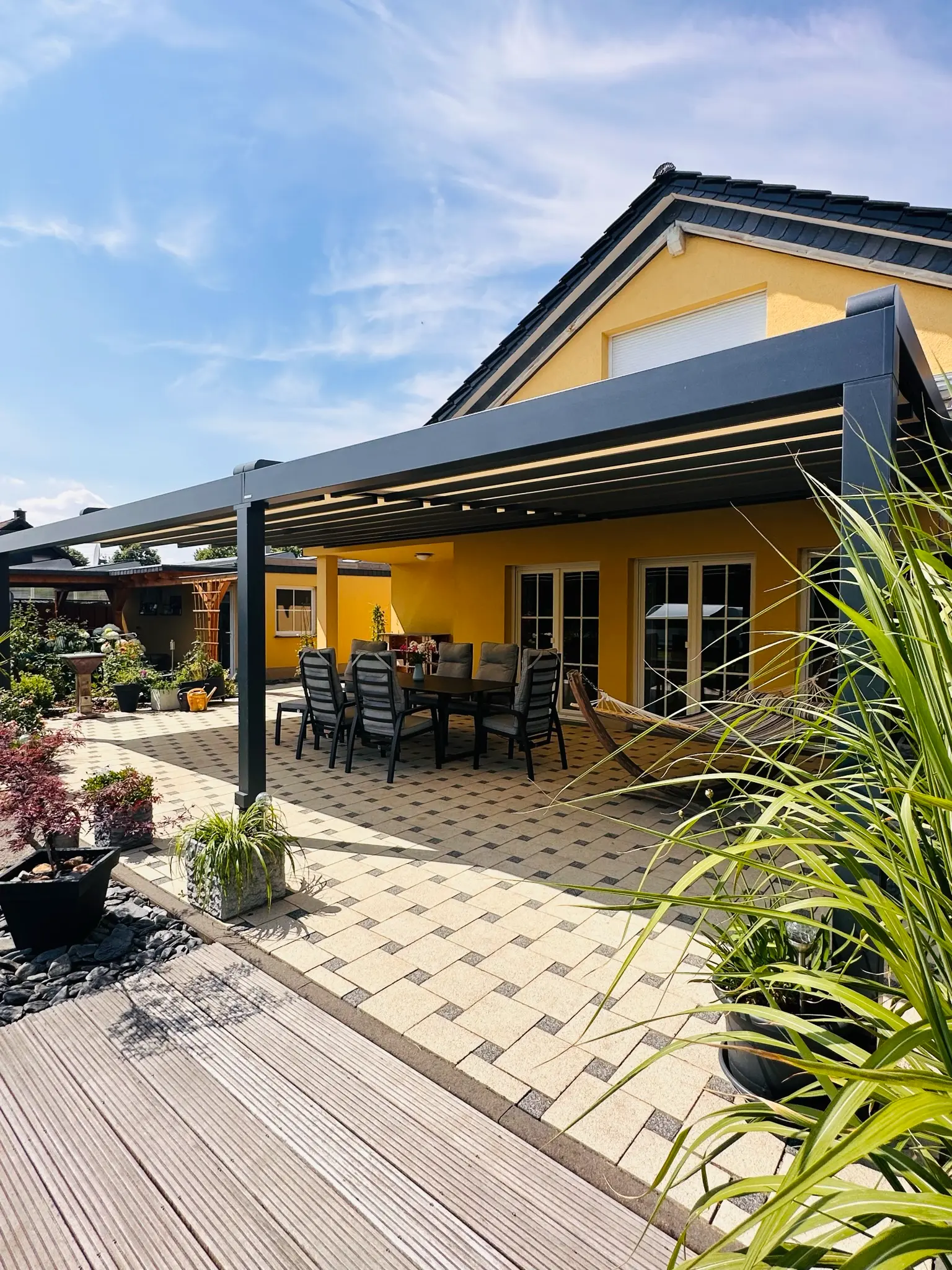 Verstellbares Lamellendach über einer großen Terrasse an einem gelben Einfamilienhaus