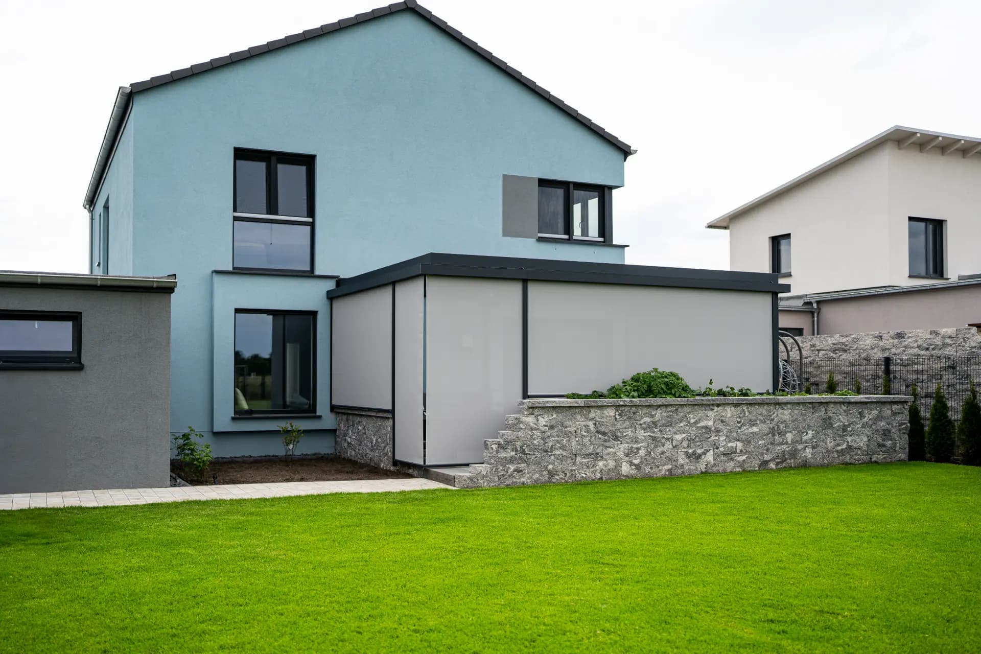 Terrassendach mit seitlichem Sichtschutz-Screen an einem hellblauen Haus
