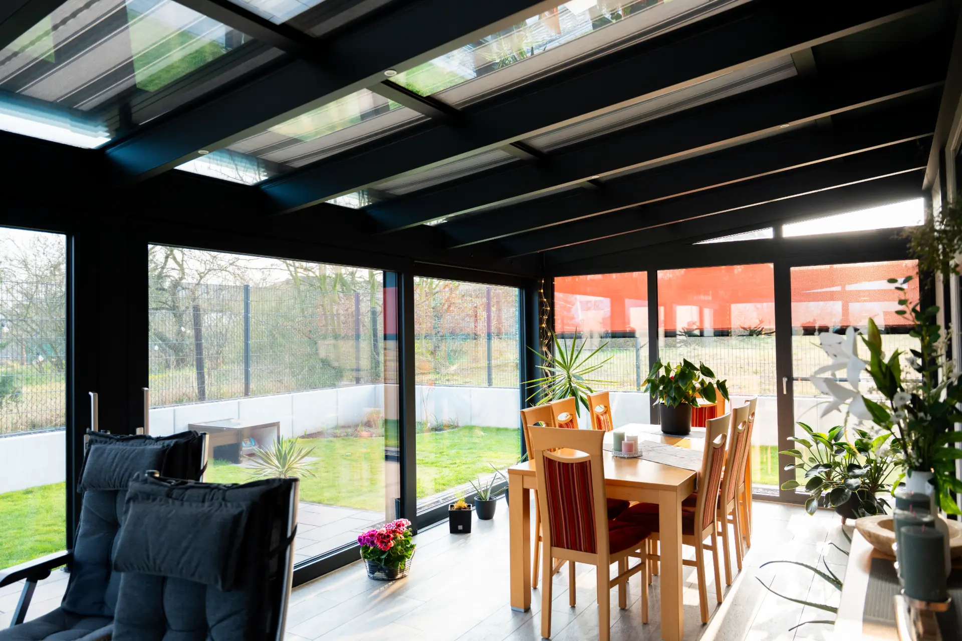 Blick aus einem verglasten Terrassenanbau in den Garten, am Fenster ein heruntergefahrener roter Sonnenschutz-Screen
