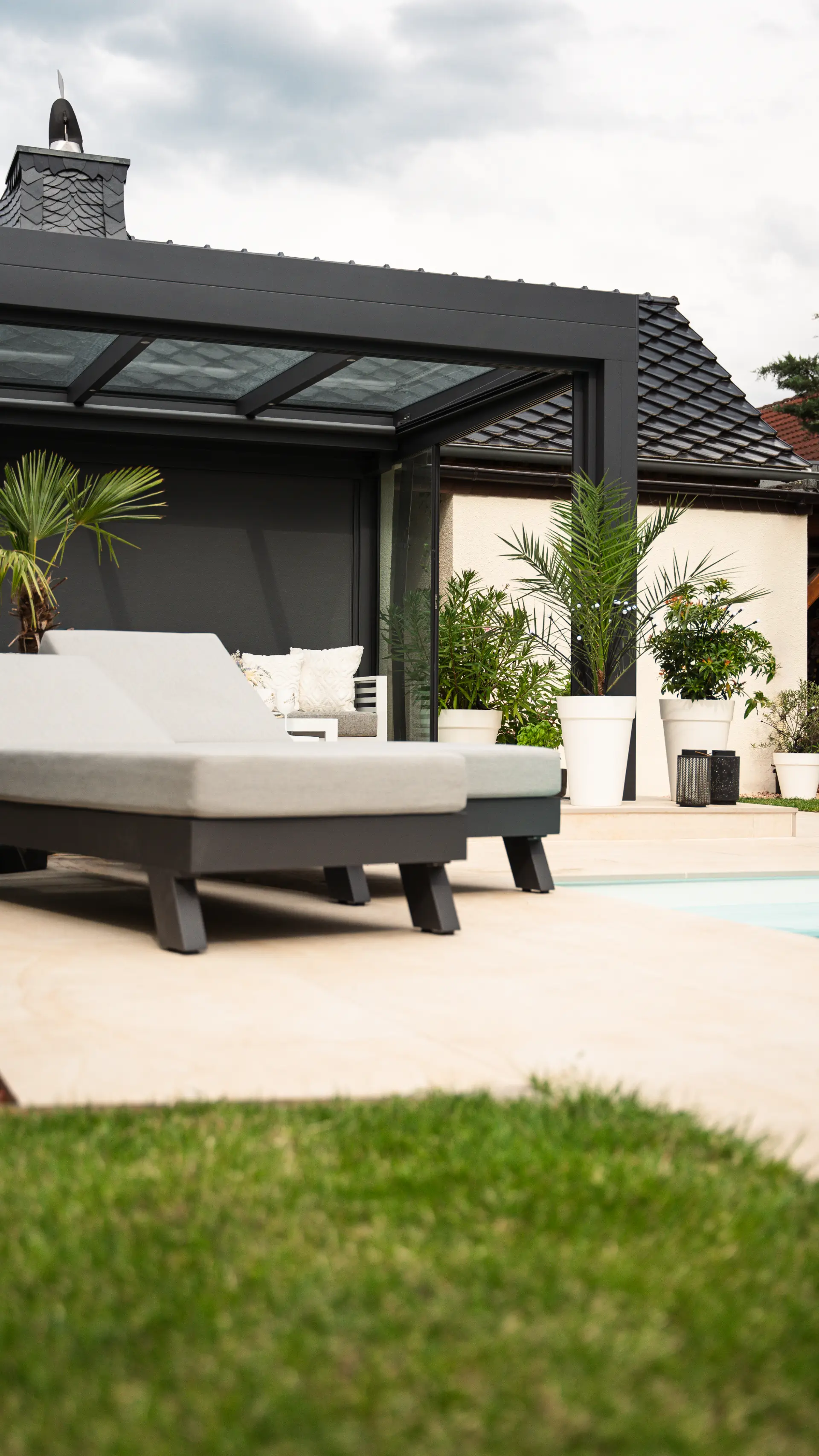 Loungebereich unter einem Terrassendach mit Palmen in weißen Kübeln und Sonnenliegen