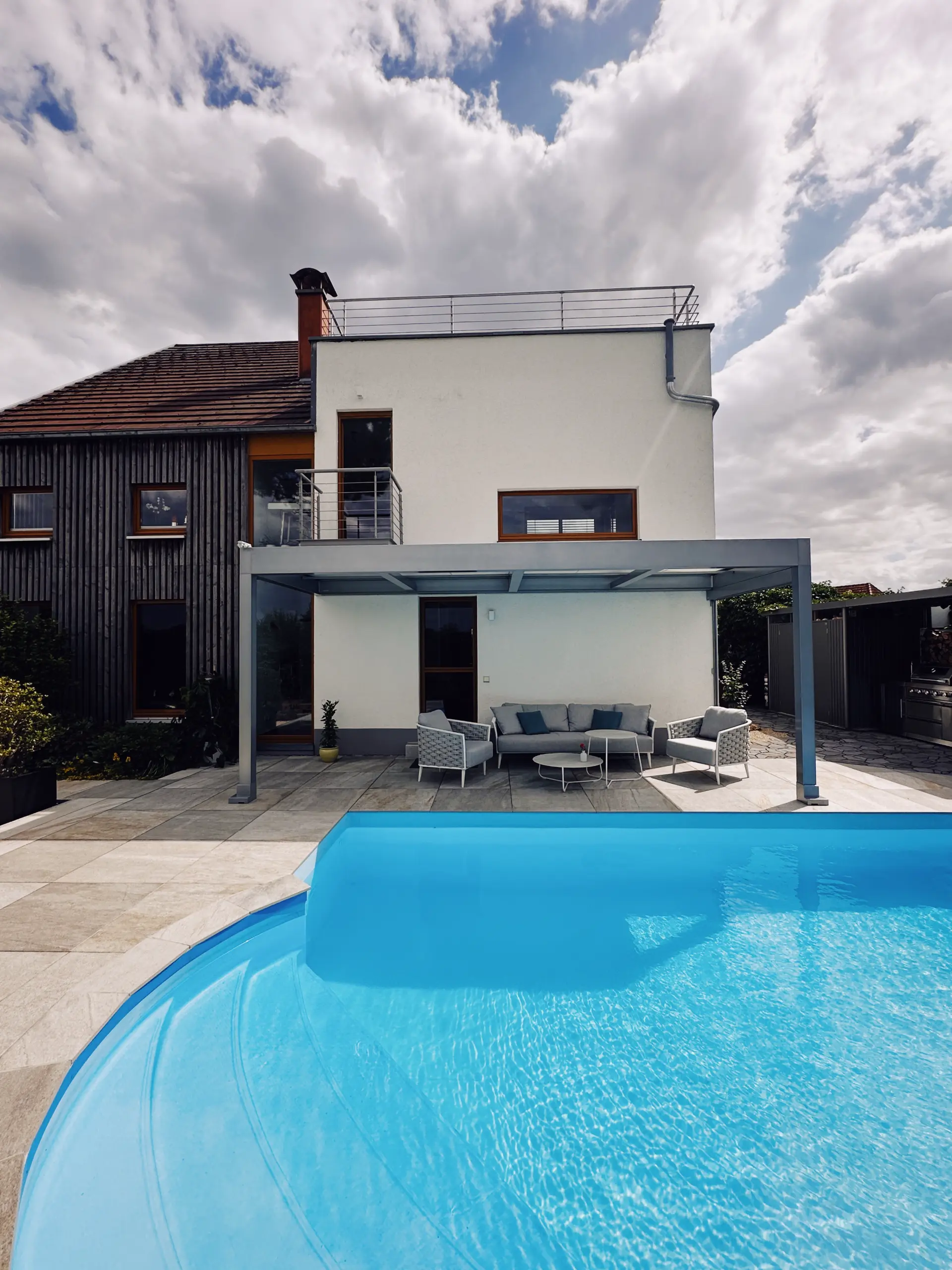 Terrassendach über einem Loungebereich an einem modernen Wohnhaus, davor ein Pool